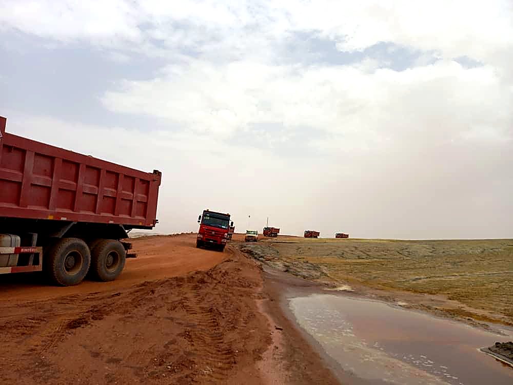 Camions bennes EMHL circulant sur une piste après la pluie