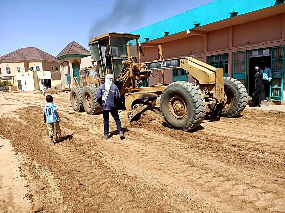Niveleuse EMHL en travaux de voirie devant des bâtiments
